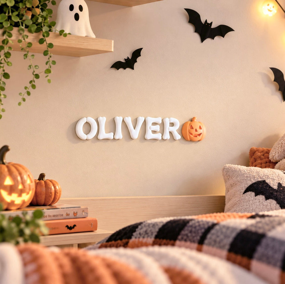 Personalized Halloween kids room decor with white 3D bone letters spelling OLIVER and an orange pumpkin accent displayed on a bedroom wall.