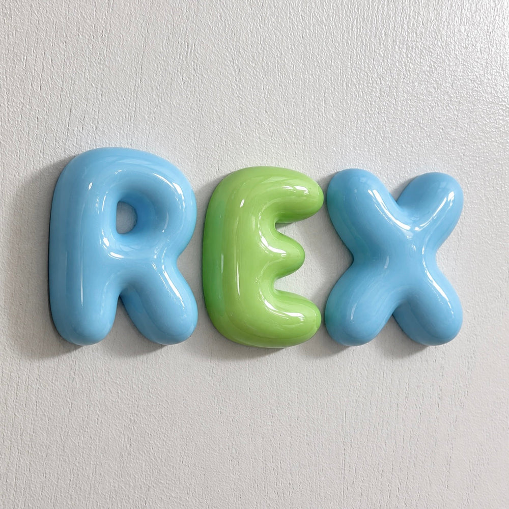 Glossy blue and green 3D bubble letters spelling REX mounted on a wall.