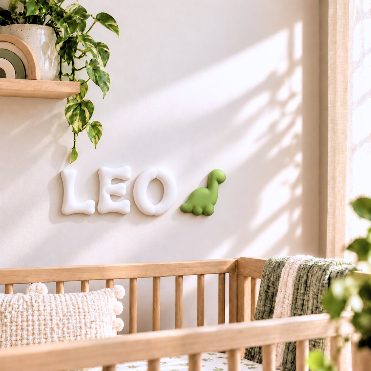 Personalized 3D dinosaur name sign with white LEO letters and green dinosaur in a soft neutral nursery above a wooden crib