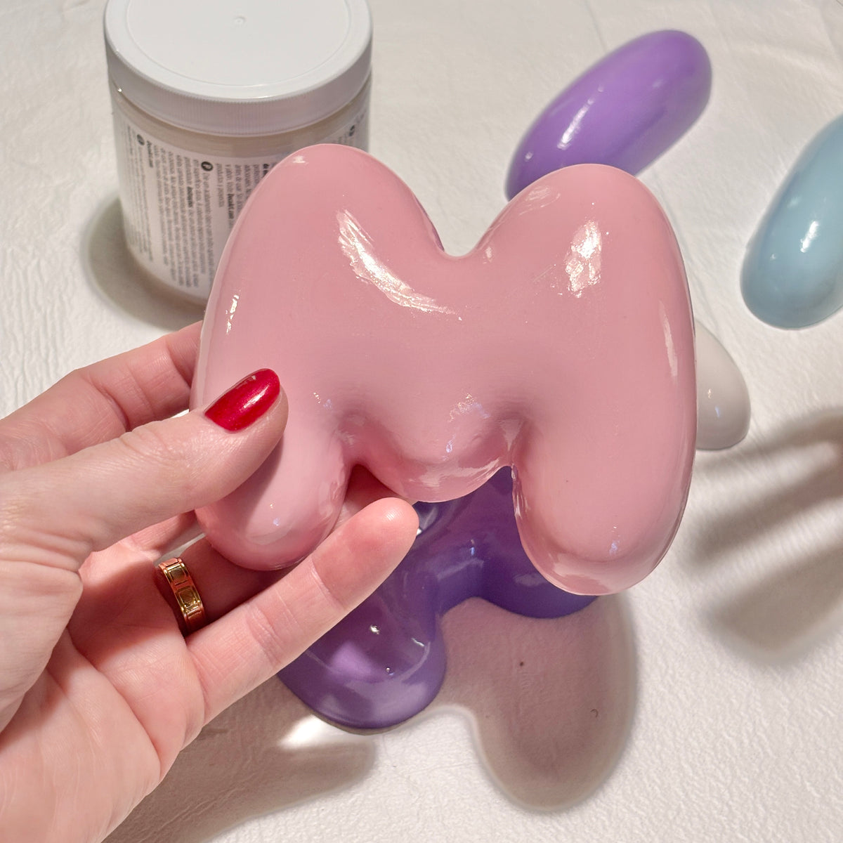 Hand holding a glossy pink 3D bubble letter M with finished letters in the background