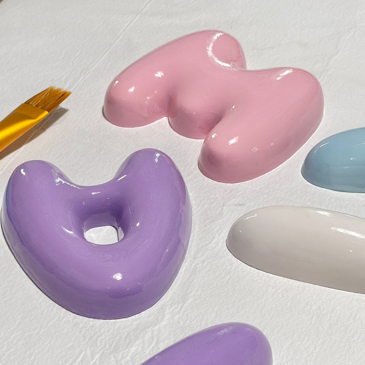 Pink, white and purple 3D bubble letters drying after their hand-finished glossy coating