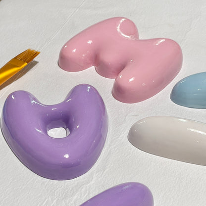 Pink, white and purple 3D bubble letters drying after their hand-finished glossy coating