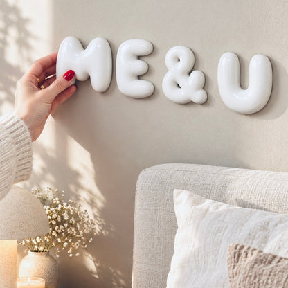 Hand installing glossy white ME & U 3D bubble letters on a neutral wall